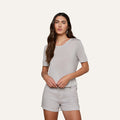 Woman with long brown hair wearing the Remy Tee in light gray, styled with matching shorts, standing against a plain light background.