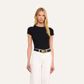 A woman with long blonde hair wears the Ressi Fitted Tee in black, paired with white pants, a black and gold belt, and gold earrings, standing against a plain light background.