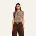 Wearing the bestselling Ressi Fitted Tee with a brown houndstooth pattern, a woman with long brown hair pairs it with wide-leg brown pants featuring white stitching and a belted waist, standing against a plain light background.