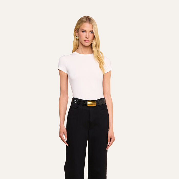 A woman with long blonde hair wears the form-fitting Ressi Fitted Tee in white, tucked into high-waisted black pants with a black belt; she stands against a plain light background.