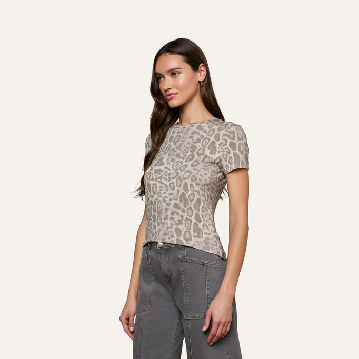 A woman stands looking to the side, wearing the bestselling Ressi Fitted Tee in gray leopard print stretch jersey knit and high-waisted gray jeans, set against a plain light background.