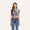 A woman with long brown hair wears the Ressi Fitted Tee in midnight blue paisley, styled with blue jeans, a brown belt, and hoop earrings as she stands against a plain light background.