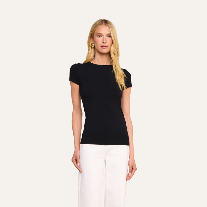 A woman with long blonde hair wears the form-fitting black Ressi Fitted Tee and white pants, standing against a plain light background.