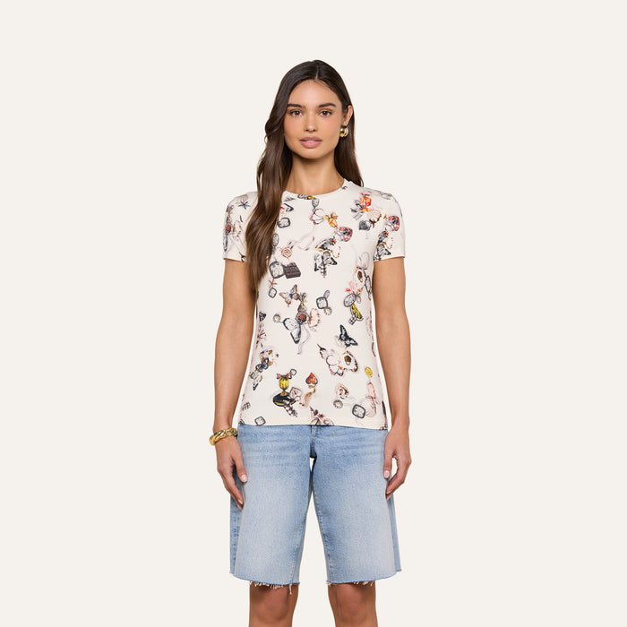 Wearing the Ressi Fitted Tee—a bestselling white T-shirt featuring a colorful print and crafted from slim-cut, stretch jersey knit—a woman stands facing forward against a plain, light background, paired with light blue knee-length denim shorts.