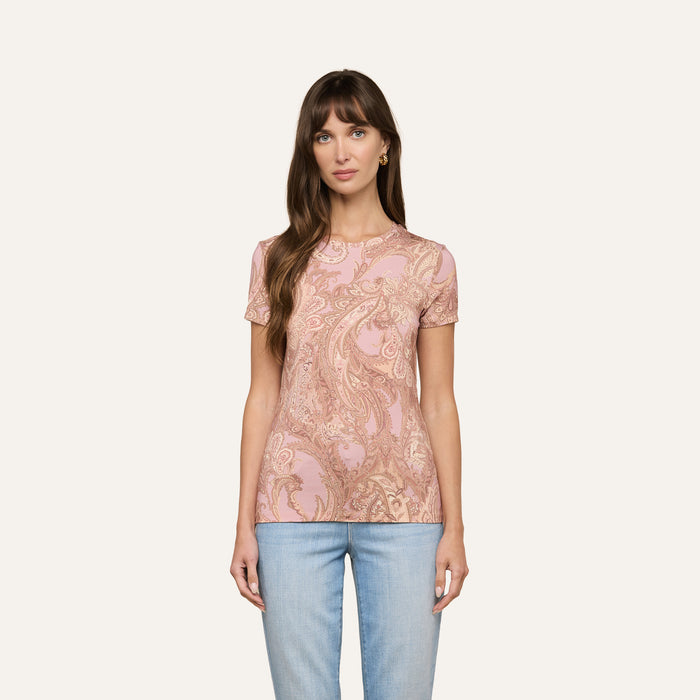 A woman with long brown hair is wearing the bestselling Ressi Fitted Tee in a mauve paisley print stretch jersey knit and light blue jeans, standing against an off-white background.