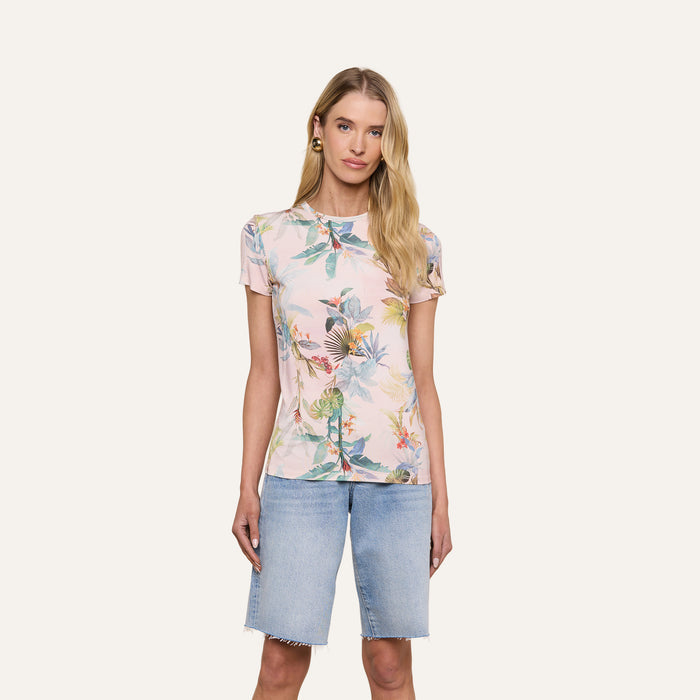 A woman wearing the bestselling Ressi Fitted Tee with a pastel floral print and light blue denim Bermuda shorts stands against a plain white background, looking at the camera with a neutral expression.