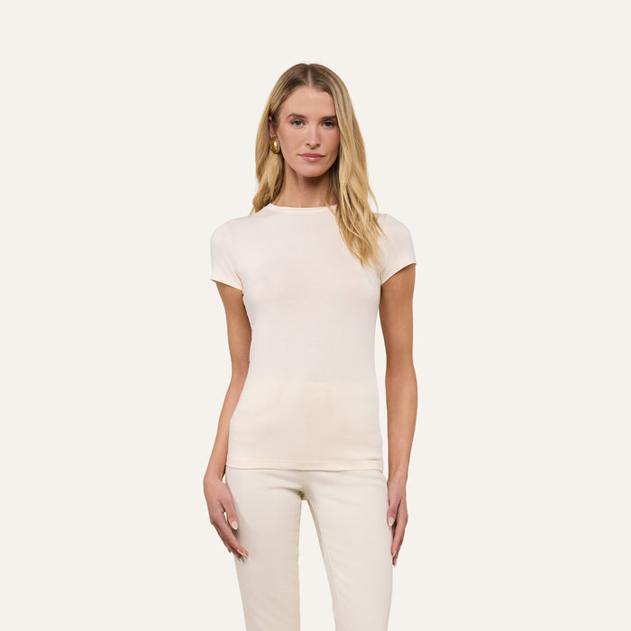 A woman with long blonde hair stands against a plain, light background, facing forward with a neutral expression, wearing the Ressi Fitted Tee in vintage white and matching pants.