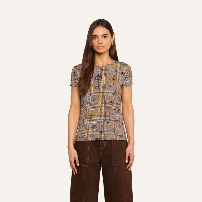 A woman with long brown hair wears the Ressi Fitted Tee—a short-sleeve, slim cut patterned top—paired with brown pants, standing against a plain light background, facing forward with her arms relaxed at her sides.