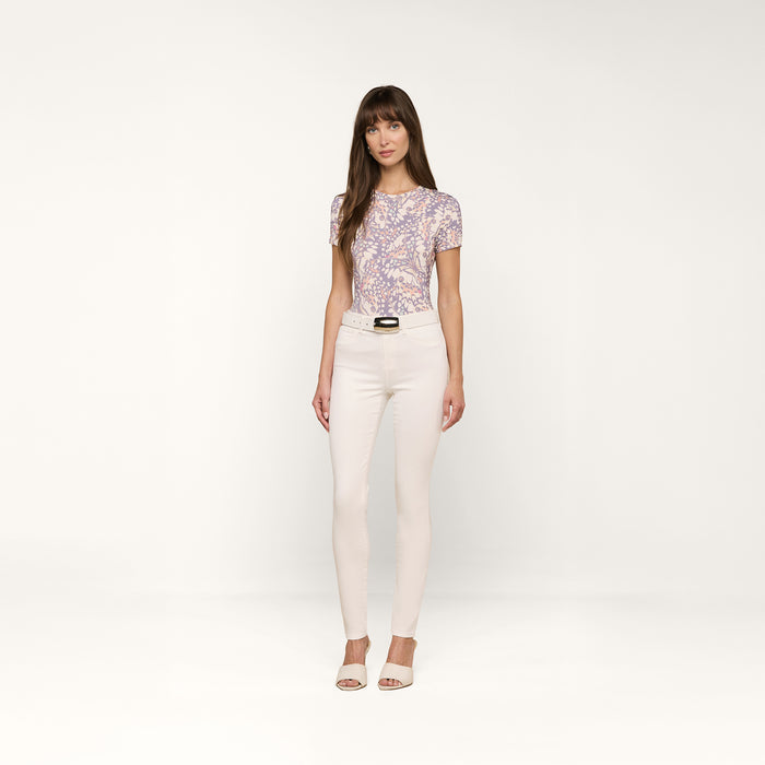 A woman stands in a studio against a plain white background, looking at the camera with a neutral expression. She wears the Ressi Fitted Tee featuring a butterfly wing print, paired with light-colored fitted pants and open-toe heels.