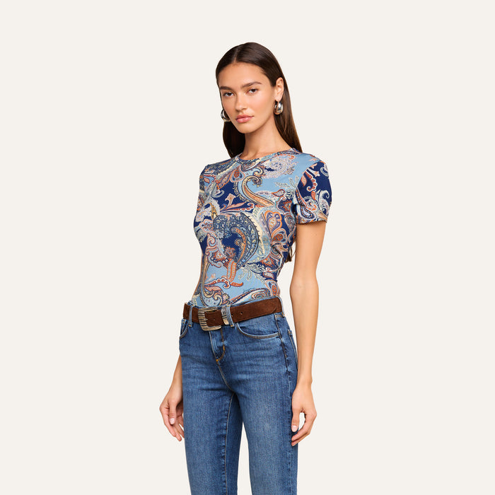 Woman wearing the Ressi Fitted Tee in midnight blue paisley, paired with blue jeans and a brown belt, standing with her arms relaxed at her sides against a plain light background.