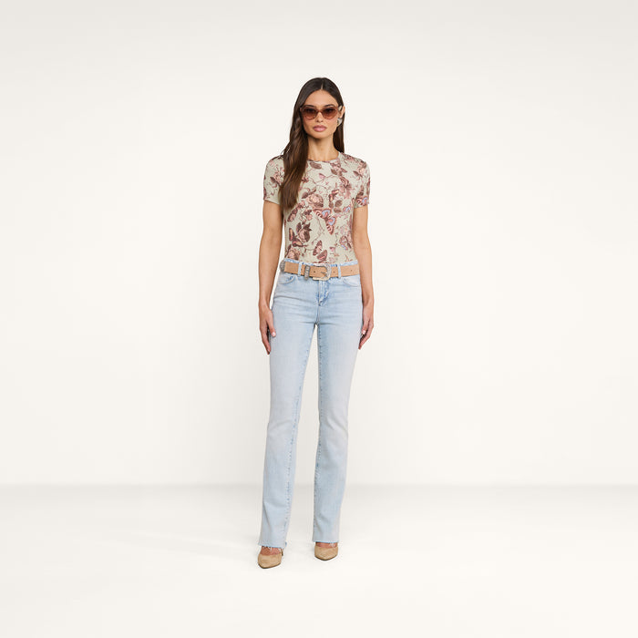 A woman stands facing forward against a plain white background, wearing sunglasses, heels, a belt, light blue jeans, and the Ressi Fitted Tee—a slim cut short-sleeve patterned top.
