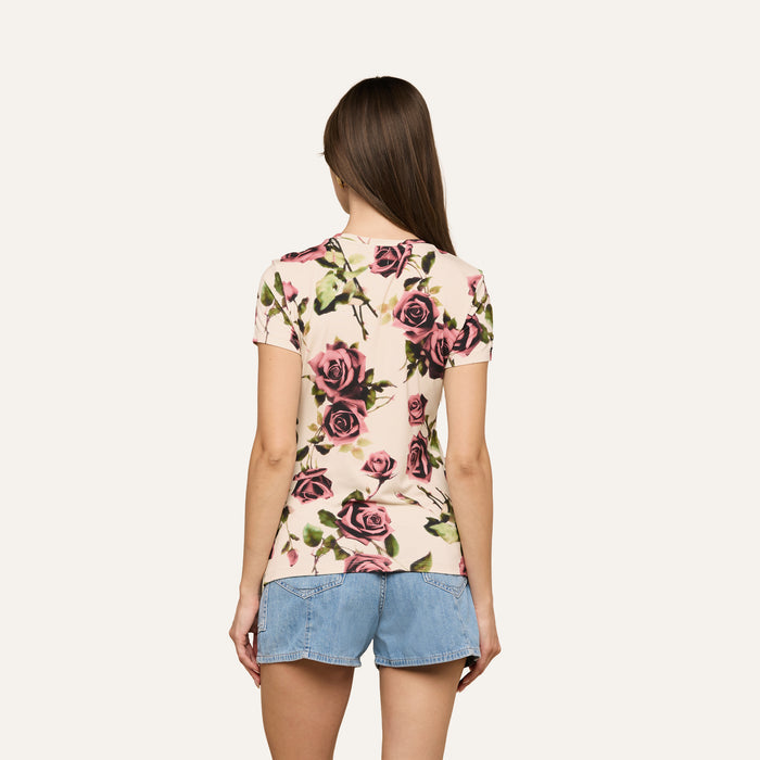 A person with long brown hair wears the Ressi Fitted Tee, a slim-cut, rose-patterned short-sleeve T-shirt made from stretch jersey knit, paired with denim shorts, standing with their back to the camera against a light background.