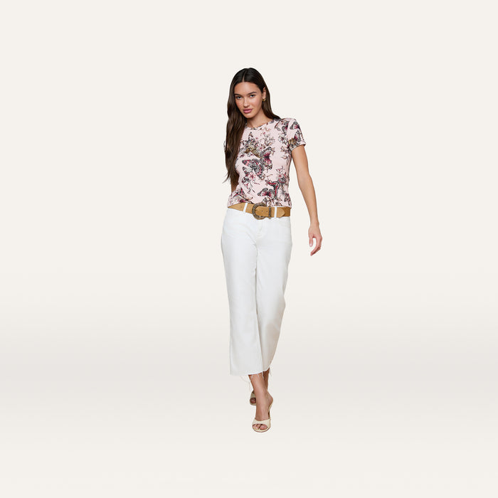 Woman wearing the bestselling Ressi Fitted Tee with a butterfly jungle print, white wide-leg pants, beige belt, and open-toe heels stands against a plain, light background.