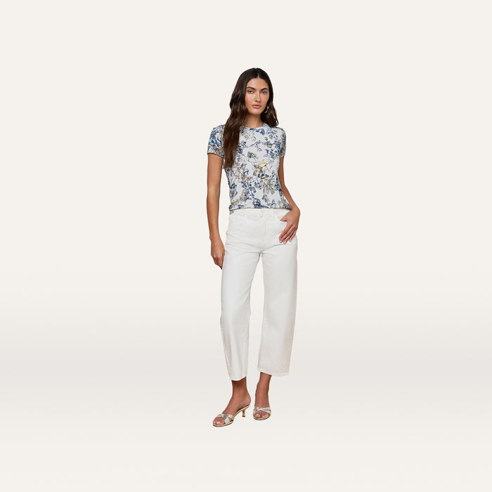 Wearing the bestselling Ressi Fitted Tee with a blue butterfly print, white cropped pants, and open-toe heels, the woman stands against a plain light background, posing with one hand in her pocket.