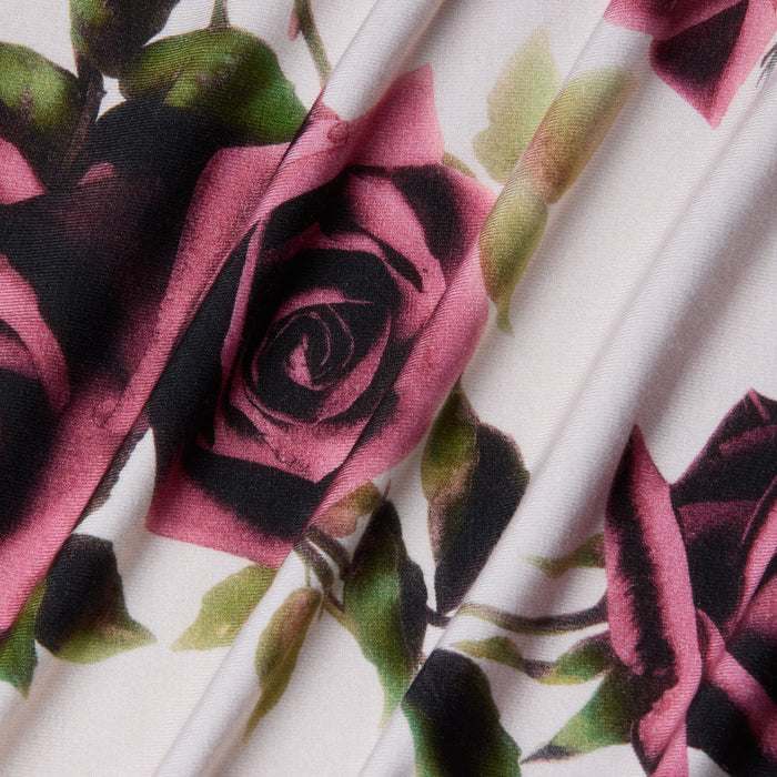 Close-up of the Ressi Fitted Tee’s stretch jersey knit fabric, featuring a printed pattern of pink and dark roses with green leaves on a light background, shown with soft folds that create subtle shadows and texture.