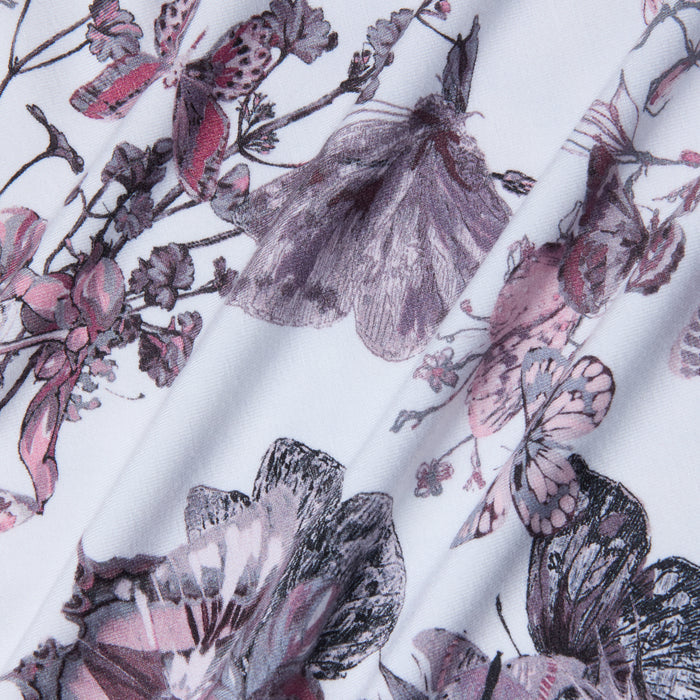 Close-up of the Ressi Fitted Tee in vintage white, featuring a detailed, artistic print of butterflies and flowers in shades of pink, purple, and gray. The fabric is slightly folded, creating soft shadows.