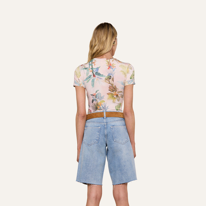 A woman stands with her back to the camera, wearing the slim-fit Ressi Fitted Tee in a pastel floral pattern and light blue denim Bermuda shorts, set against a plain, light-colored background.