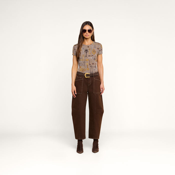 A woman wearing sunglasses, the bestselling Ressi Fitted Tee with a patterned short-sleeve design, brown high-waisted wide-leg pants, and brown boots stands facing forward against a plain white background.
