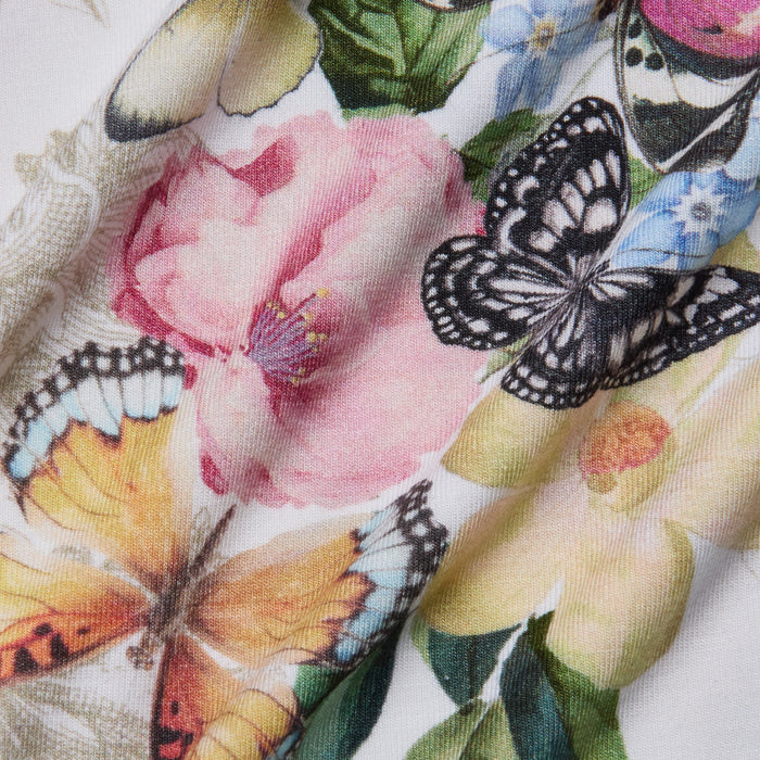 Colorful butterflies rest on large, detailed flowers in pink, yellow, and blue on a slightly wrinkled stretch jersey knit, creating a vibrant butterfly garden print inspired by nature on the Ressi Fitted Tee.