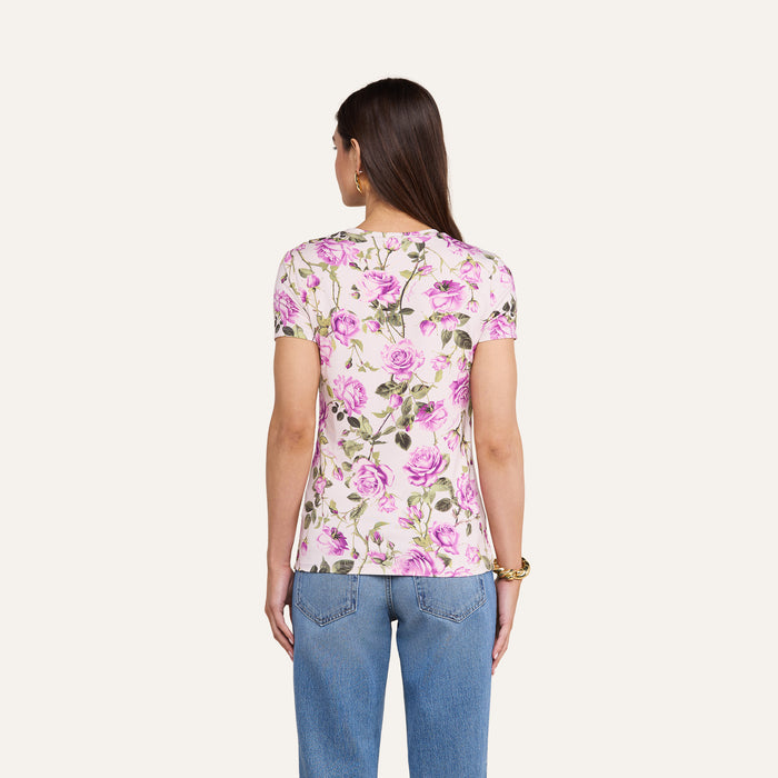 A woman stands with her back to the camera, wearing the bestselling Ressi Fitted Tee in white with a pink and green floral pattern, paired with light blue jeans, against a plain light background.