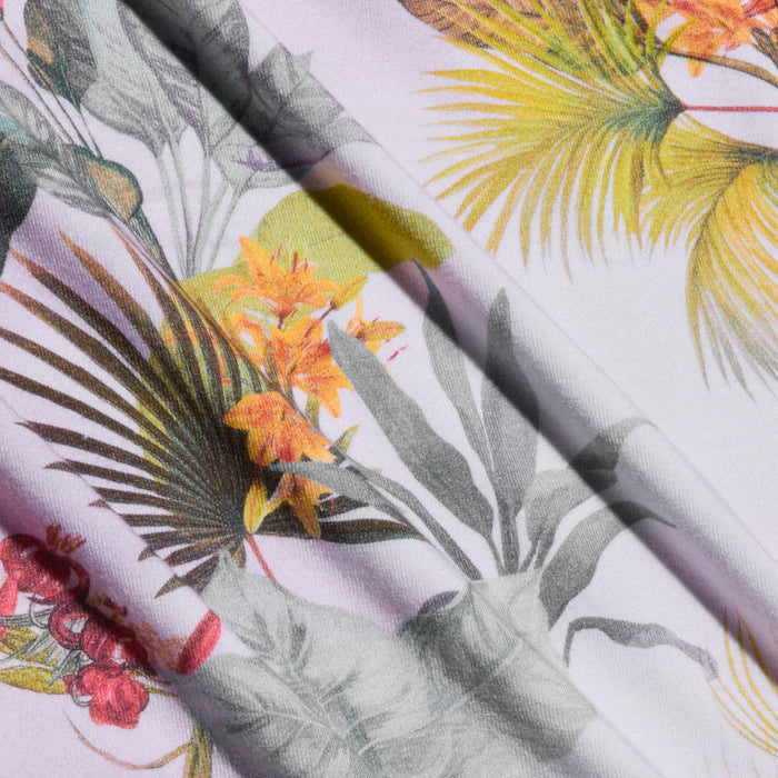 Close-up of the Ressi Fitted Tee, showcasing fabric with a palm leaf print and tropical floral pattern—featuring green palm leaves, orange and yellow flowers, plus hints of red and gray on a light background. The tee’s fabric displays soft folds and gentle shadows.