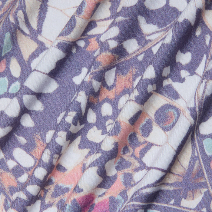 A close-up of the Ressi Fitted Tee’s stretch jersey knit fabric displays abstract geometric shapes in muted purple, white, pink, and teal, complemented by soft folds and creases.