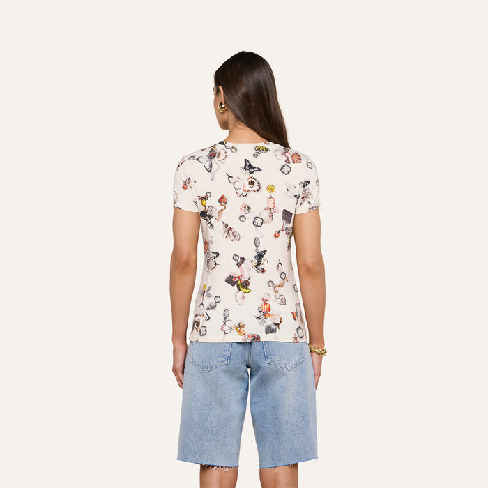 A person with long brown hair wears the bestselling Ressi Fitted Tee in printed white stretch jersey knit and light blue knee-length denim shorts, standing with their back to the camera against a plain light background.