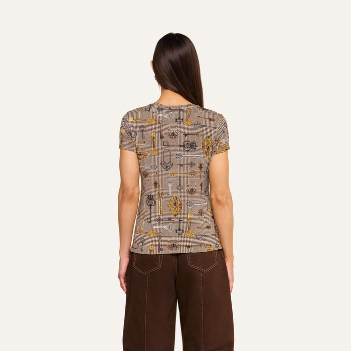 A person with long brown hair stands facing away, wearing the bestselling Ressi Fitted Tee and brown houndstooth pants against a plain light background.