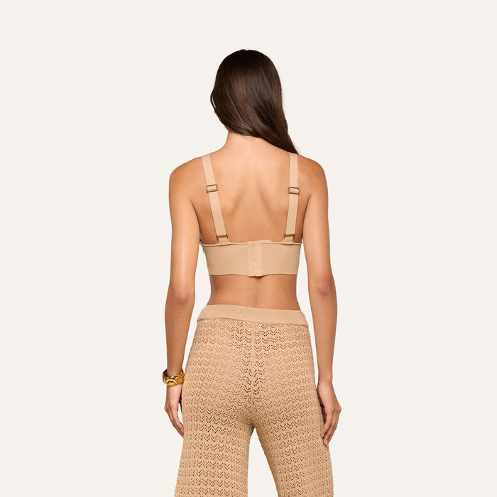 A woman with long brown hair is shown from the back, wearing the Reverie Pointelle Knit Bralette and high-waisted, light brown pointelle knit pants. Her arms are relaxed by her sides against a plain background.