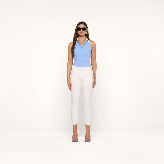 A woman wearing sunglasses, the Rina Poplin Halter Top in light blue organic cotton, white high-waisted pants, and sandals stands facing forward against a plain white background.