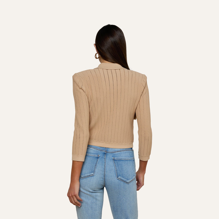A woman with long brown hair, wearing the Risa Collared Cardigan in beige and light blue jeans, stands facing away from the camera against a plain light background.