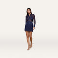 Wearing the Riven Lace Mini Skirt, a woman in a navy floral lace long-sleeve shirt and matching midnight blue ensemble strides forward in high-heeled sandals against a plain white background.