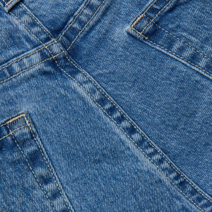 Close-up view of blue denim fabric showing detailed stitching and seams, likely part of the River Jean Bermuda Short, with visible pocket and seam lines.