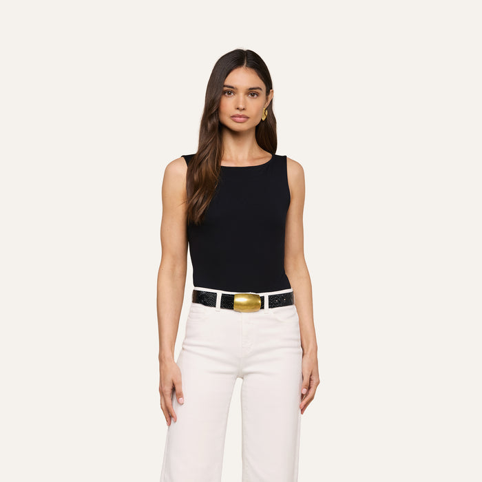 Woman with long brown hair wearing the sleeveless L’AGENCE Riza Boatneck Bodysuit, paired with white pants and a white belt featuring a large gold buckle, standing against a plain light background.