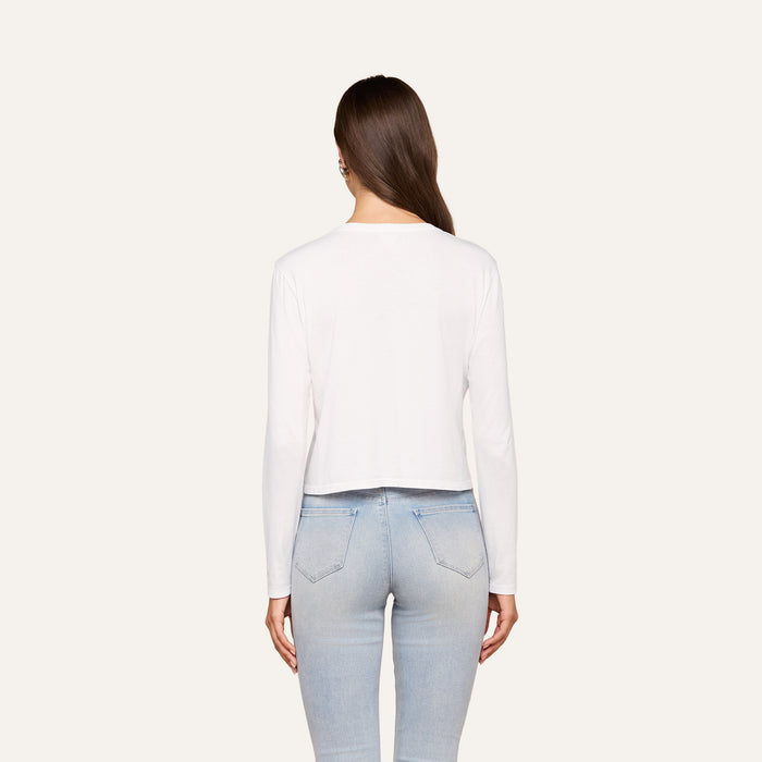A woman stands with her back to the camera, wearing the Rojene Cotton Tee in a relaxed fit paired with light blue jeans, set against a plain light background.