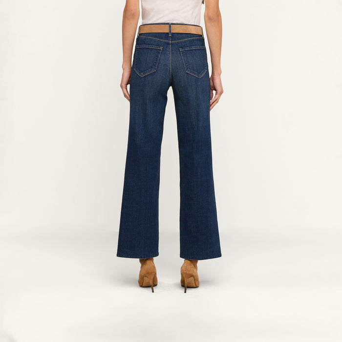 A person stands facing away, wearing the Rosalyn Wide-Leg Jean in high-rise, dark blue stretch denim with tan heels against a plain white background.