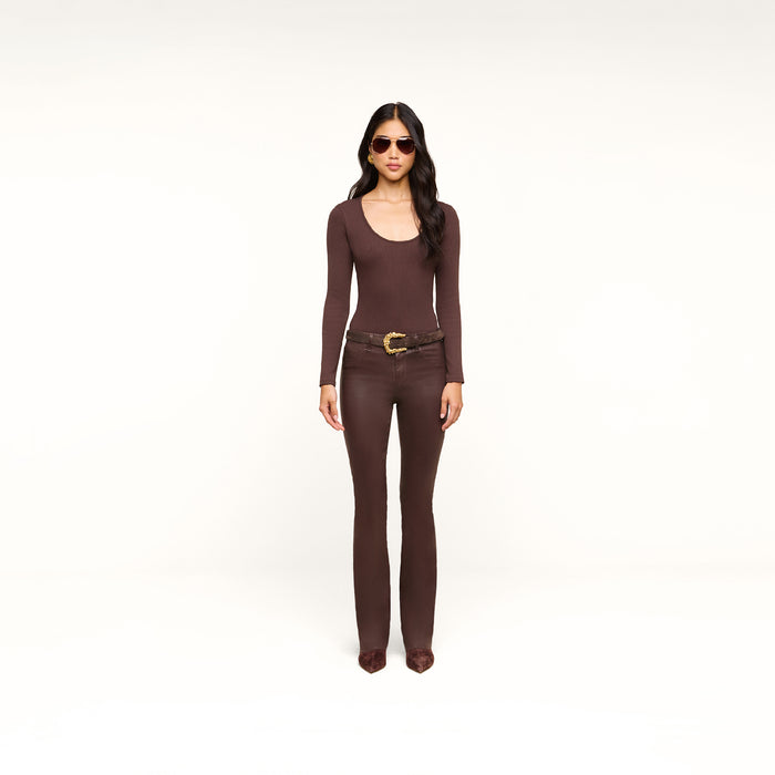A woman wearing sunglasses, a fitted brown long-sleeve top, the Ruth Coated Straight-Leg Jean with a raw hem, and pointed shoes stands facing forward against a plain white background.