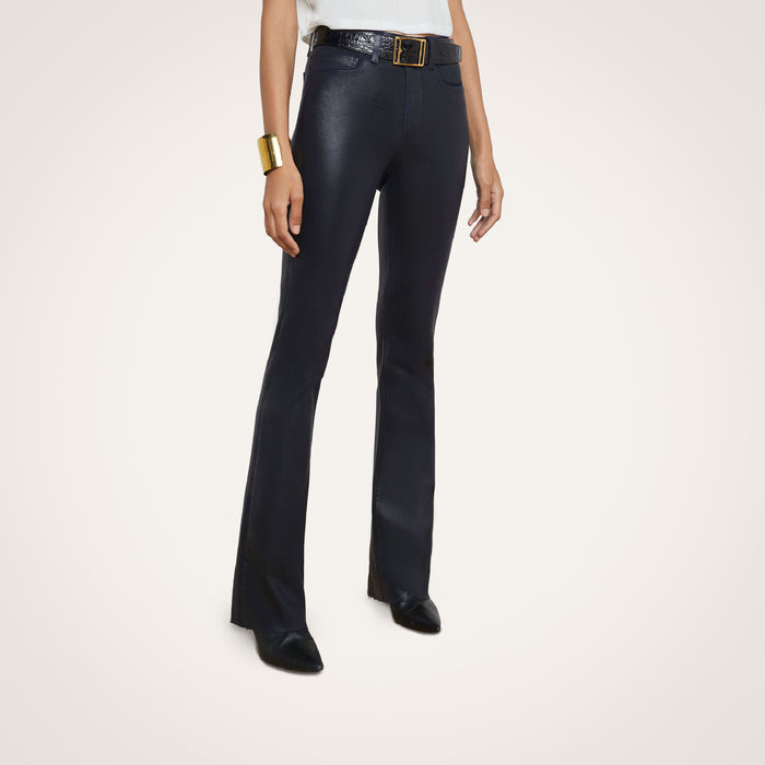 A person wearing the Ruth Coated Straight-Leg Jean with a belt and black shoes, paired with a white top and gold bracelet, stands against a plain light background.