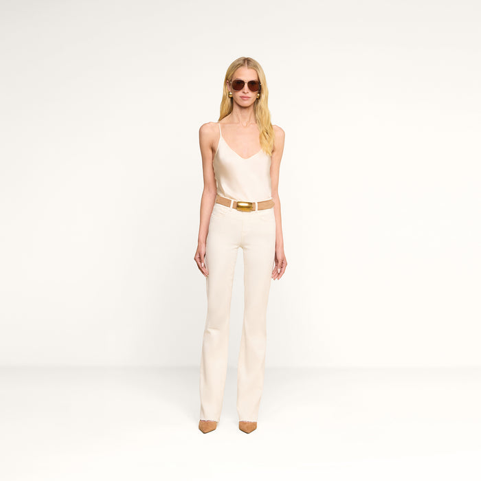 A woman wearing sunglasses, a beige camisole, the Ruth Straight-Leg Jean in stretch denim with a belt, and brown pointed-toe heels stands against a plain white background.