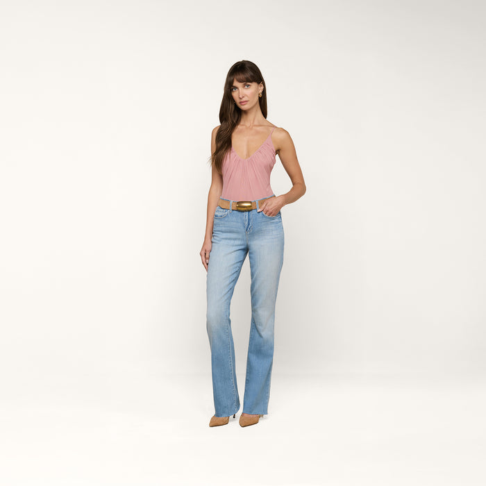 A woman stands against a plain white background wearing a pink sleeveless top, the Ruth Straight-Leg Jean in light indigo wash with a raw hem, a brown belt, and brown pointed shoes.