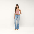 A woman stands against a plain white background wearing a pink sleeveless top, the Ruth Straight-Leg Jean in light indigo wash with a raw hem, a brown belt, and brown pointed shoes.