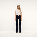 A woman stands facing forward against a plain white background, wearing a fitted white t-shirt, the Ruth Straight-Leg Jean in ultra dark indigo wash with a wide belt, and black shoes.