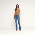 A woman wearing sunglasses, a tan sleeveless top, the Ruth Straight-Leg Jean in indigo with a raw hem, a brown belt, and heeled sandals stands against a plain white background.