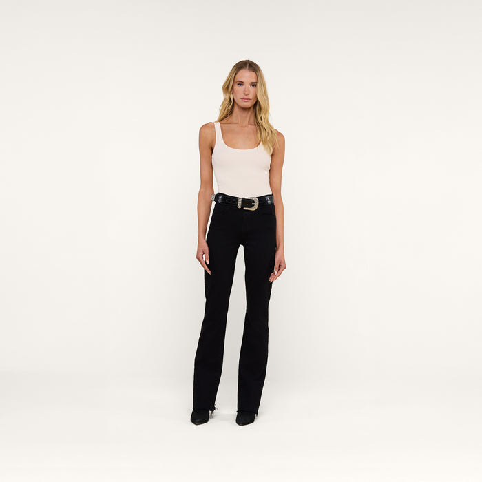 A woman with long blonde hair stands facing forward against a plain white background, wearing a light tank top, a black belt, black shoes, and high-rise black Ruth Straight-Leg Jeans.