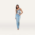 A woman stands against a plain, light background wearing the Ruth Straight-Leg Jean in a vintage wash, paired with a blue and white patterned spaghetti strap top and heeled sandals.
