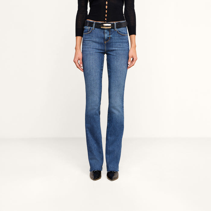 Wearing the Ruth Straight-Leg Jean in a medium indigo wash, styled with a black belt, black pointed shoes, and a black long-sleeve top, the model is shown from shoulders down against a plain white background.