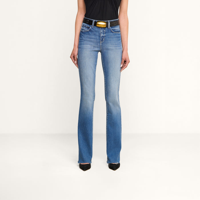 Person wearing Ruth Straight-Leg Jean in light blue—crafted from premium stretch denim—paired with a black sleeveless top, a black belt featuring a gold buckle, and black pointed shoes, standing against a plain white background.