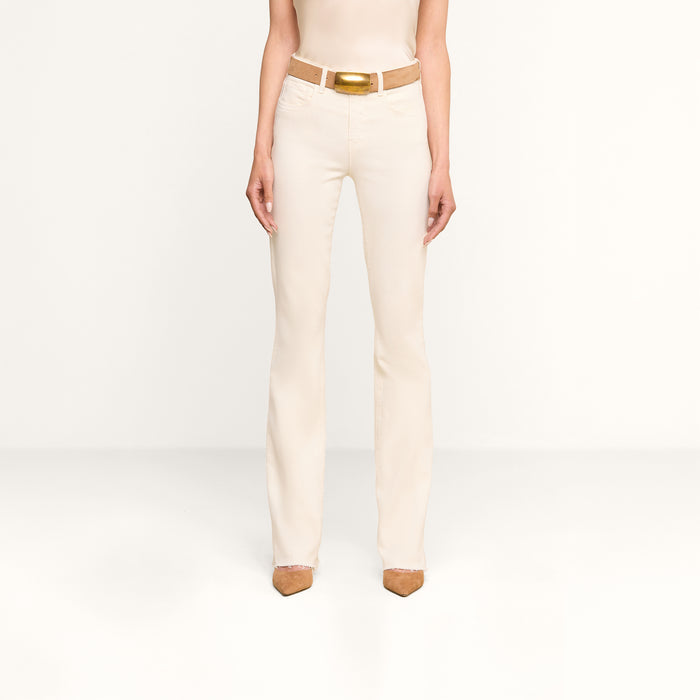 A person stands facing forward, wearing the Ruth Straight-Leg Jean in vintage white, styled with a matching cream-colored tank top, a tan belt, and brown pointed-toe shoes against a plain white background.