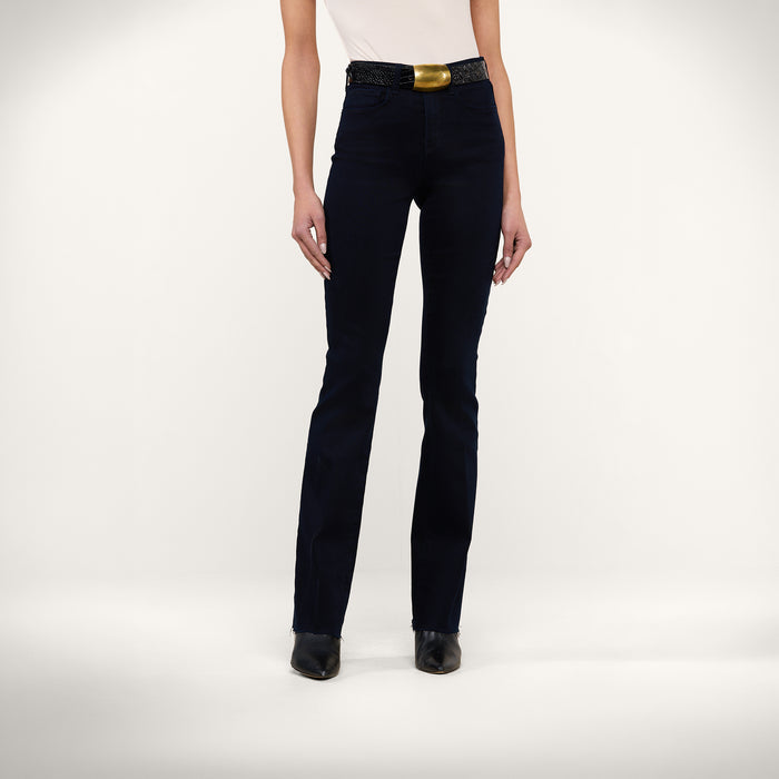 A person is wearing a white sleeveless top, the Ruth Straight-Leg Jean in an ultra dark indigo wash, a black belt with a gold buckle, and black pointed shoes, standing against a plain light background.