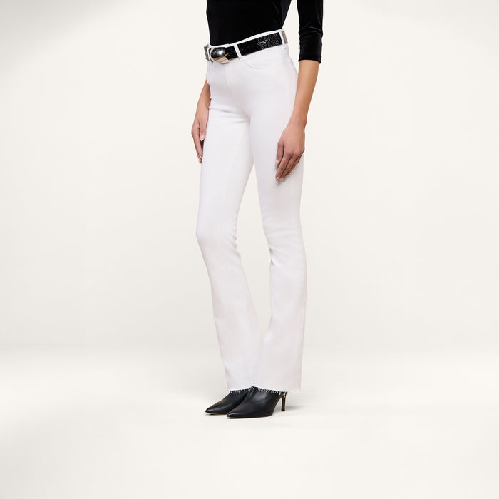 A person wearing the Ruth Straight-Leg Jean in white stretch denim, styled with a black belt, a black long-sleeve top, and black pointed-toe heels stands in front of a plain white background.